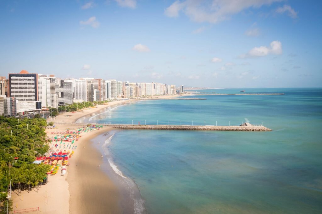 Vista aérea da Praia de Meireles, em Fortaleza, com o calçadão, barracas coloridas e prédios ao fundo.