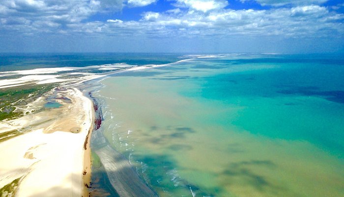 Vista aérea de Jericoacoara, com o mar em tons de azul se fundindo ao azul do céu.