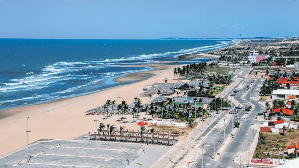 Vista aérea da Praia do Futuro, com o mar azul se destacando e os coqueiros e as barracas na orla.