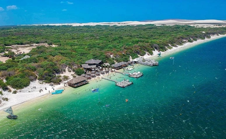 Vista aérea da Praia do Preá, com o mar azul e calmo se destacando diante da mata e do horizonte.