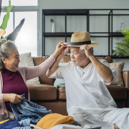 old asian senior couple packing cloth and stuff for a trip together,happiness asian old age retired mature adult enjoy arrange cloth together on floor at living room at home interior background