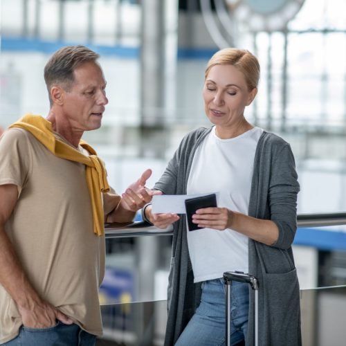 Focused middle-aged Caucasian male passenger pointing at the boarding ticket in his female companion hands